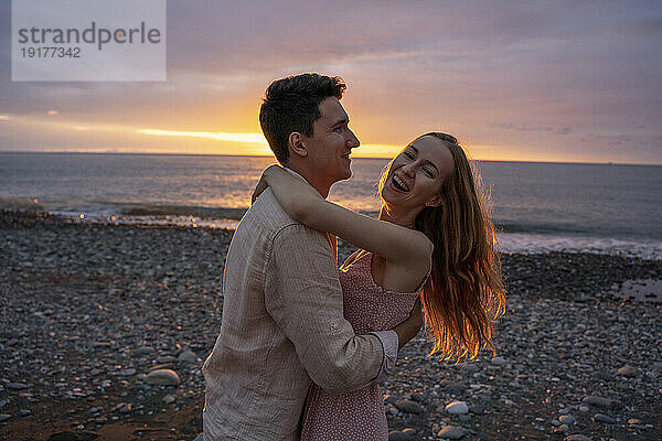 Glückliches junges romantisches Paar tanzt am Strand bei Sonnenuntergang