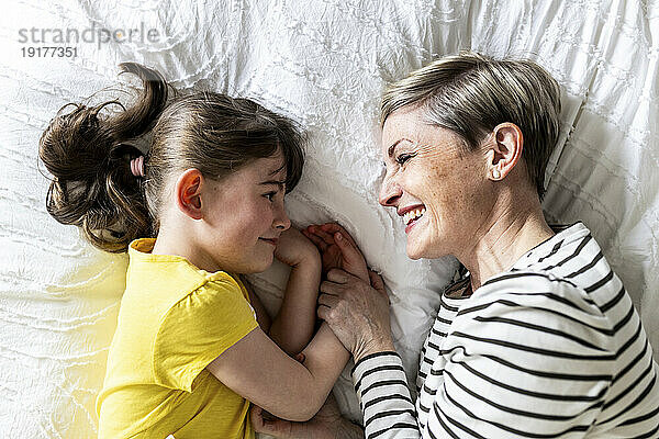 Smiling mother and daughter relaxing on bed in bedroom
