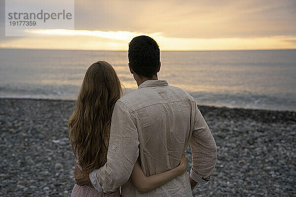 Junger Mann und Frau mit Armen um das Meer am Strand genießend