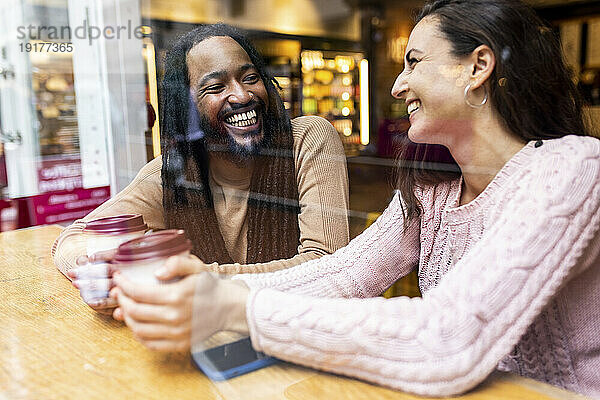 Glückliches gemischtrassiges Paar  das mit Kaffeetassen im Café sitzt