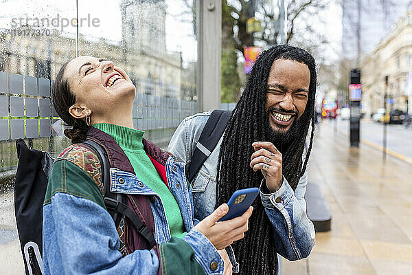 Fröhlicher Mann und Frau halten Smartphone in der Hand und lachen über Fußweg