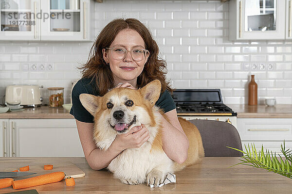 Lächelnde Frau mit walisischem Corgi-Hund in der Küche