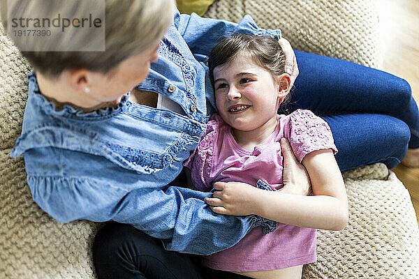 Smiling girl lying on mother's lap sitting on sofa
