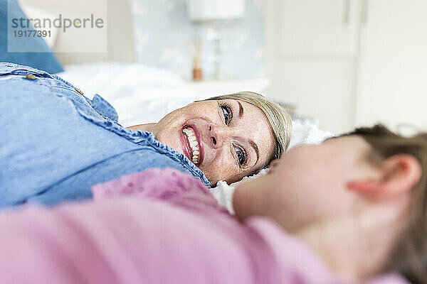 Smiling mother lying with daughter on bed in bedroom
