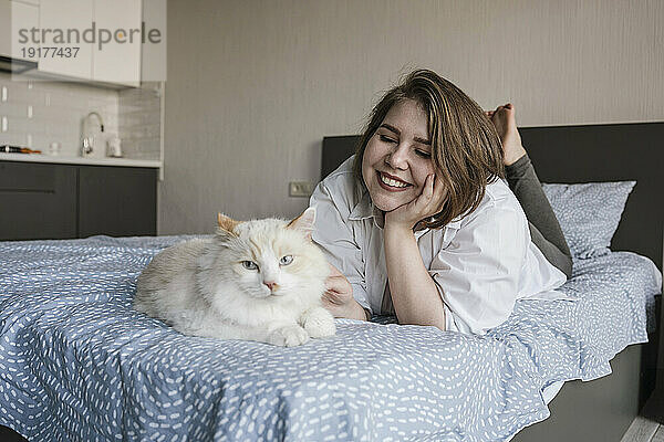 Lächelnde Frau streichelt die Katze  die auf dem Bett liegt
