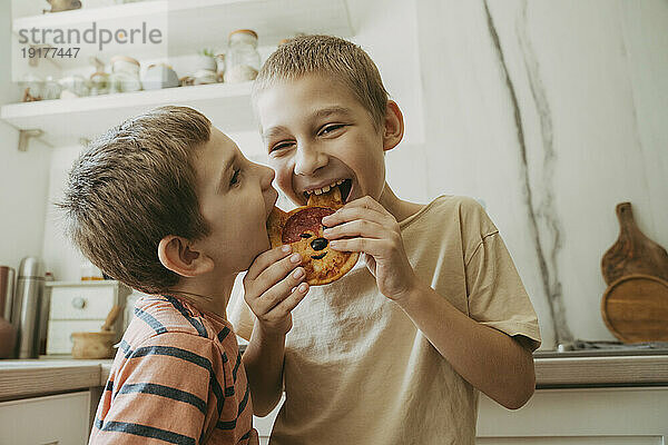 Smiling brothers eating pizza in kitchen