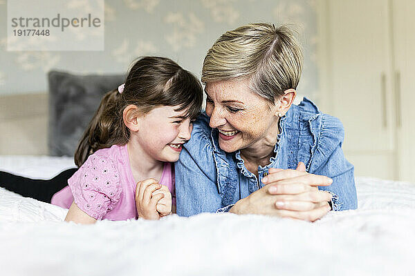 Happy daughter and girl lying on bed at home