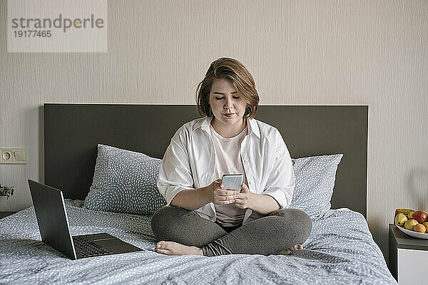 Junger Freiberufler nutzt Smartphone zu Hause im Bett