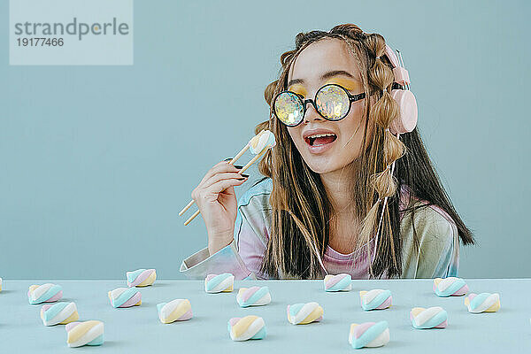 Frau mit Kaleidoskopbrille isst Marshmallows mit Stäbchen im Studio