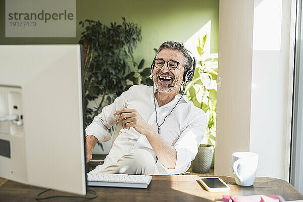Kundenbetreuer lacht und redet über Headset im Heimbüro