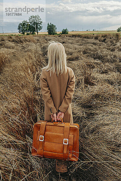 Blonde Frau läuft mit Koffer im Feld