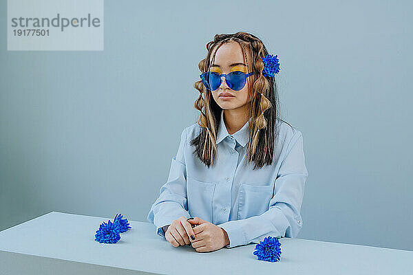 Nachdenkliche Frau mit Sonnenbrille und blauen Blumen am Tisch im Studio