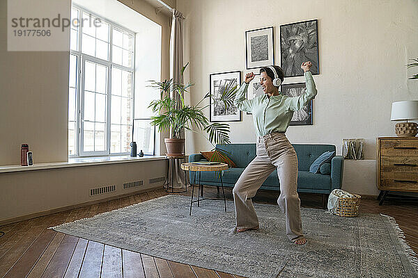 Fröhliche Frau mit kabellosen Kopfhörern tanzt zu Hause