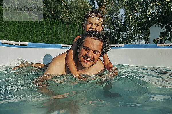 Glücklicher Vater trägt seinen Sohn zurück im Pool