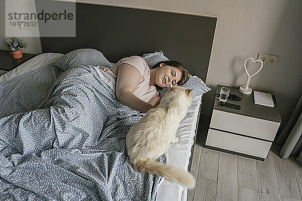 Happy woman relaxing with cat on bed at home