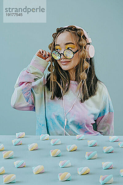 Woman with kaleidoscope and headphones sitting near marshmallows on table in studio