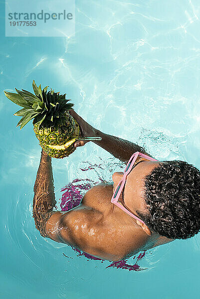 Man holding pineapple in swimming pool on sunny day