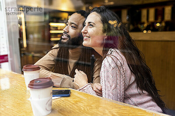 Lächelnder Mann und Frau mit Kaffeetassen sitzen am Tisch im Café