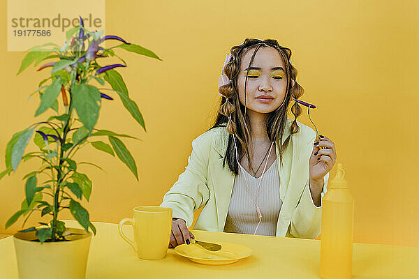 Junge Frau isst Pfeffer am Tisch vor gelbem Hintergrund