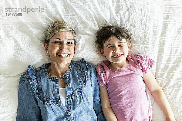 Smiling mother and daughter lying on bed