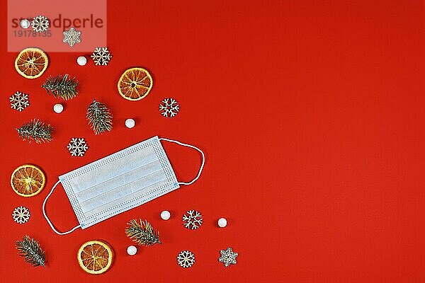 Konzept für Weihnachten zur Zeit des Coronavirus mit medizinischer Gesichtsmaske  umgeben von festlichem Weihnachtsschmuck auf rotem Hintergrund mit Kopierraum
