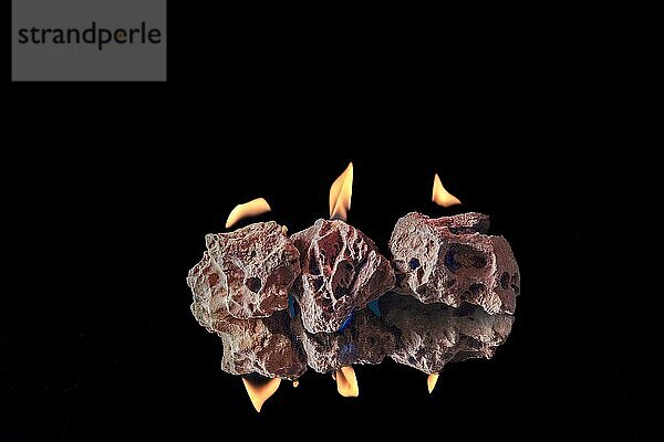 Gruppe von bunten Steinen mit Feuer Flammen auf dem Boden reflektiert vor einem schwarzen Hintergrund