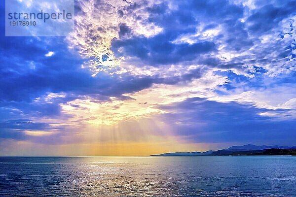 Schöne Meereslandschaft mit bunten Wolken und helle Sonnenstrahlen über ruhigen Meerwasser und dunstigen fernen Küsten geworfen. Sonnenaufgang oder Sonnenuntergang im Mittelmeer  Weichzeichner Hintergrund