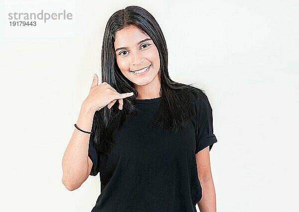 Lächelndes junges Mädchen gestikuliert Anruf mit Hand isoliert. Glückliches lateinisches Mädchen gestikuliert Anruf mit Fingern isoliert