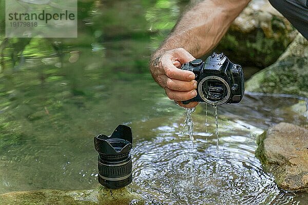 Mann zieht seine Digitalkamera aus dem Fluss  die versehentlich in den von innen überfluteten Fluss gefallen ist