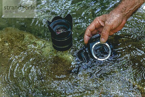 Ein Mann reinigt den Sensor seiner Spiegelreflexkamera im Wasser eines Flusses  indem er ihn von innen flutet