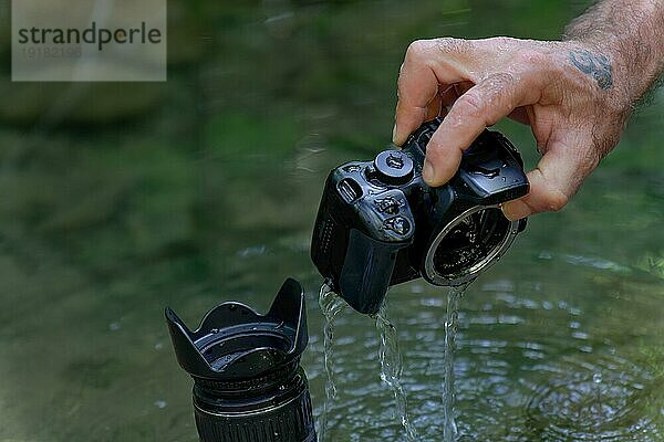 Mann zieht seine Digitalkamera aus dem Fluss  die versehentlich in den von innen überfluteten Fluss gefallen ist
