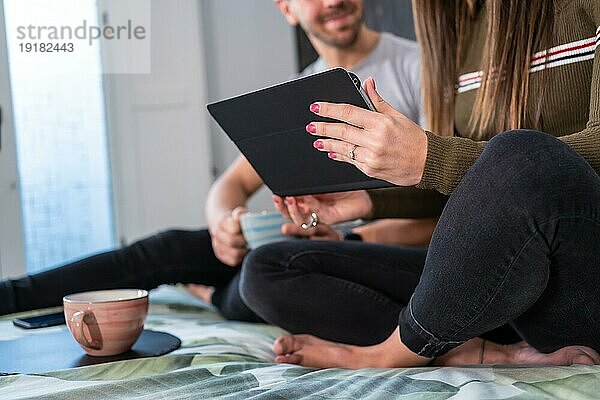 Nahaufnahme der Hände und Beine eines nicht erkennbaren Paares  das entspannt auf dem Bett ein Tablet benutzt