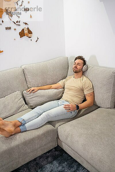 Vertikale Draufsicht auf einen Mann  der entspannt auf dem Sofa liegt und Musik hört