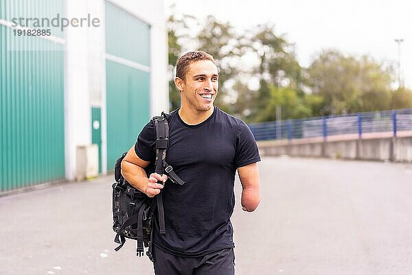 Glücklicher junger Sportler mit einem amputierten Arm bei der Ankunft im Fitnessstudio