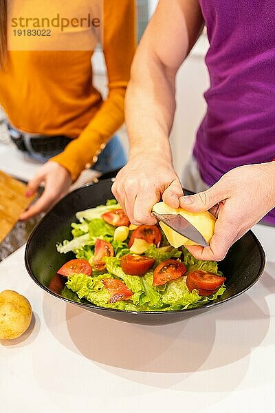 Vertikales Foto mit Nahaufnahme eines Mannes  der neben seiner Partnerin zu Hause Zutaten für einen Salat schneidet