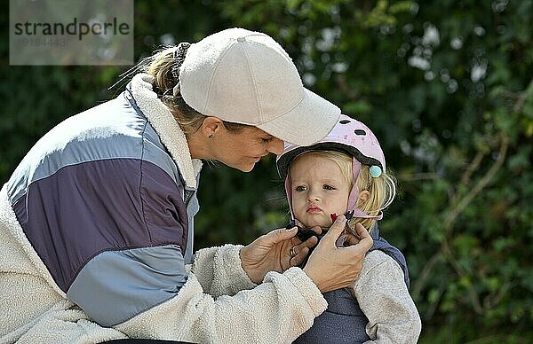 Mutter  Frau  blond  Basecap  zieht kleinem Mädchen  2 Jahre  blond  Helm  rosa  an  schließt Scharnier  Stuttgart  Baden-Württemberg  Deutschland  Europa