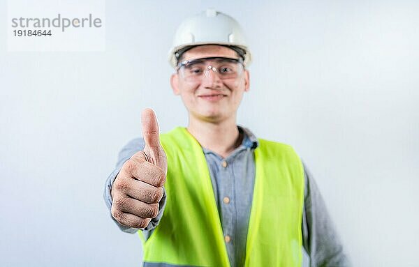 Lächelnder junger Ingenieur  der mit dem Daumen Zustimmung signalisiert. Fröhlicher Ingenieur  der der Kamera die Daumen nach oben zeigt  isoliert