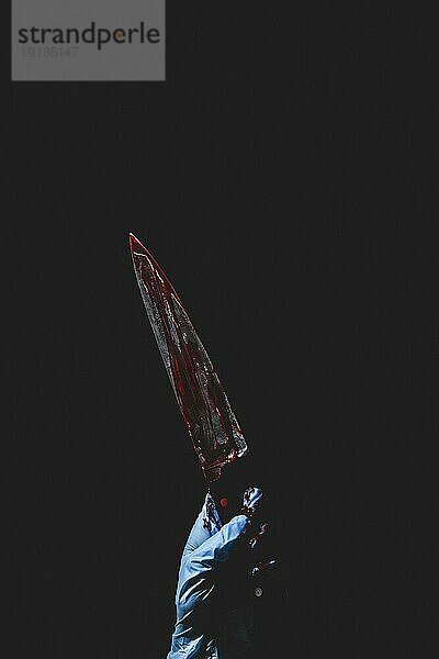 Nach oben zeigende Hand in blauem Handschuh hält blutverschmiertes Messer  dunkler Hintergrund  Halloween  Kopierraum
