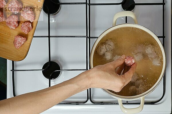 Draufsicht auf eine weibliche Hand  die Fleischbällchen in kochendes Wasser fallen lässt