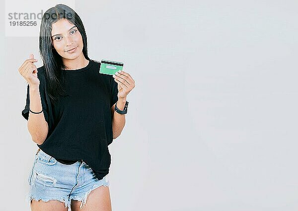 Mädchen hält eine Kreditkarte und macht eine Geldgeste mit den Fingern  isoliert  mit Blick in die Kamera