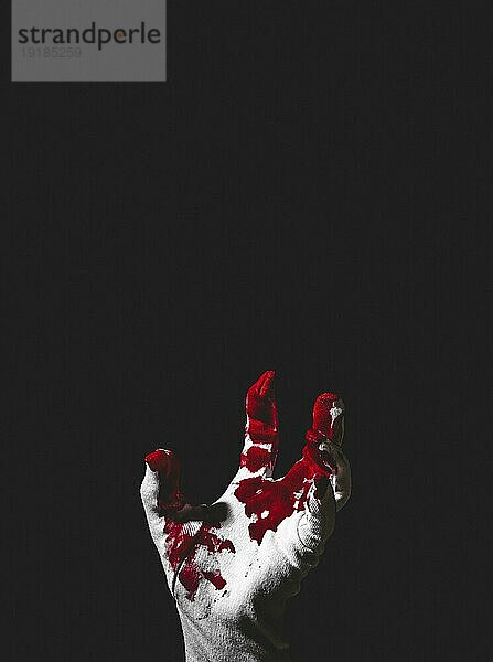 Nach oben greifende Hand in weißem Handschuh mit Blutflecken  dunkler Hintergrund  Halloween  Kopierraum