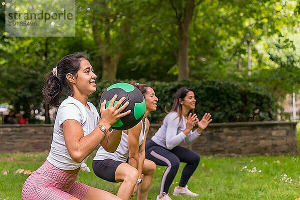 Latino Mädchen beim Sport in einem grünen Park  Lifestyle ein gesundes Leben  Lehrer mit den Schülern tun Kniebeugen mit dem Gewicht Ball
