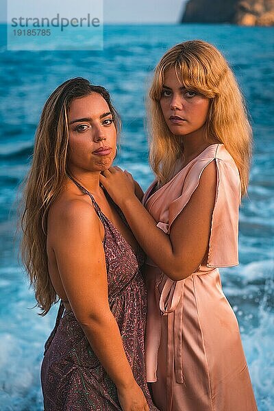 Ein paar kaukasische Mädchen in rosa Kleidern  posieren Sommer am Strand am Meer  vertikales Foto