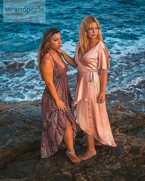 Romantische Blicke eines Paares von kaukasischen Mädchen in rosa Kleidern  posiert Sommer am Strand am Meer