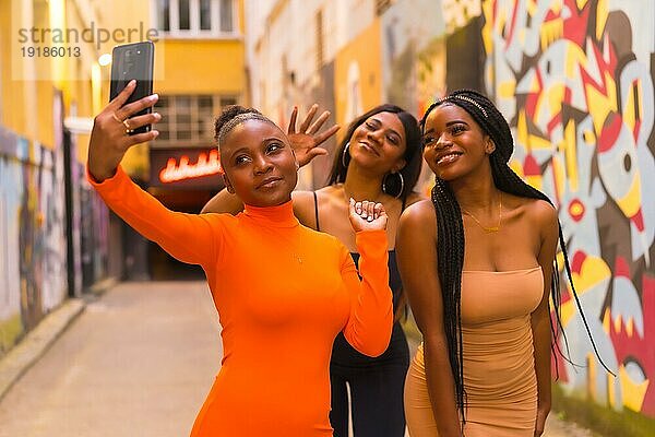 San Sebastián  Gipuzkoa Spanien  Februar 2021: Drei Mädchen machen ein Selfie. Modischer urbaner Stil mit drei schwarzafrikanischen Mädchen in engen Kleidern auf einer Stadtstraße. Girlfriends Lebensstil