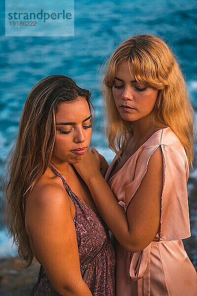 Ein paar kaukasische Mädchen in rosa Kleidern  posieren Sommer am Strand am Meer  vertikales Foto