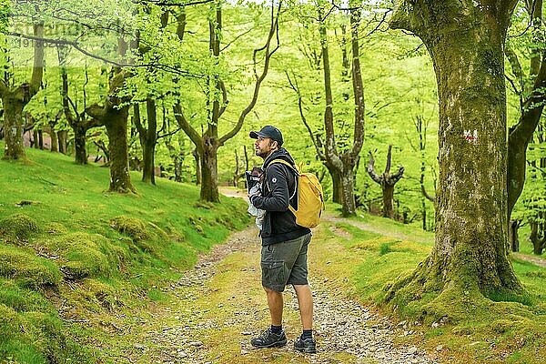 Ein junger Vater geht mit seinem neugeborenen Kind im Rucksack auf einem Waldweg zum Picknick mit der Familie