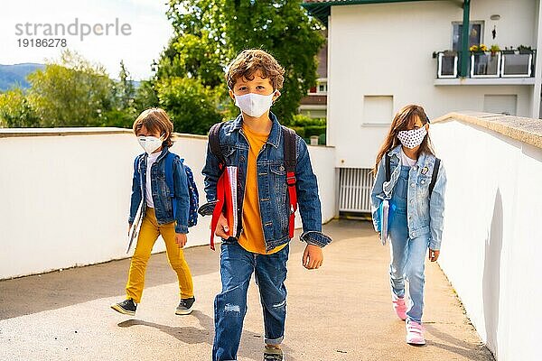 Drei Brüder mit Gesichtsmasken  bereit  wieder zur Schule zu gehen. Neue Normalität  soziale Distanz  Coronaviruspandemie Covid 19. Verlassen des Hauses mit allen Sicherheitsmaßnahmen