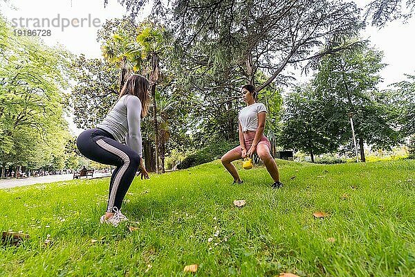 Lateinamerikanisches Mädchen  das in einem grünen Park Sport treibt  Lehrer  der den weiblichen Schülern Übungen mit Gewichten beibringt