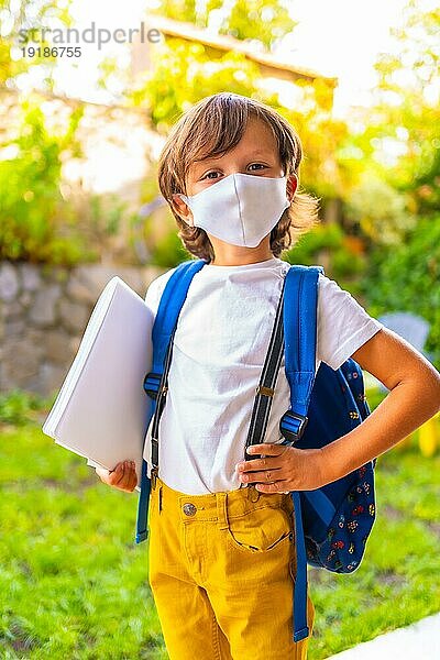 Kaukasisches Kind mit Gesichtsmaske  bereit für die Rückkehr zur Schule. Neue Normalität  soziale Distanz  Coronaviruspandemie Covid 19. In kurzen Ärmeln  mit Rucksack und einem Block für Notizen in der Hand